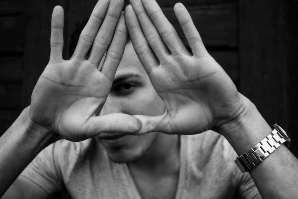 photo of young man peering through his hands shaped like a triangle