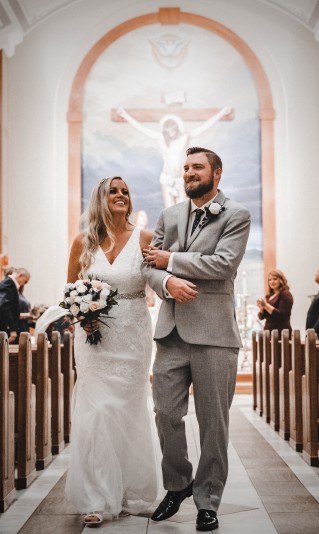 Photo of wedding couple walking out of church with crucifix in background