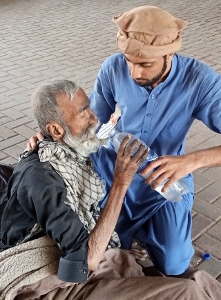 Man in blue clothing feeding an old man by Sarwar e Kainat Welfare